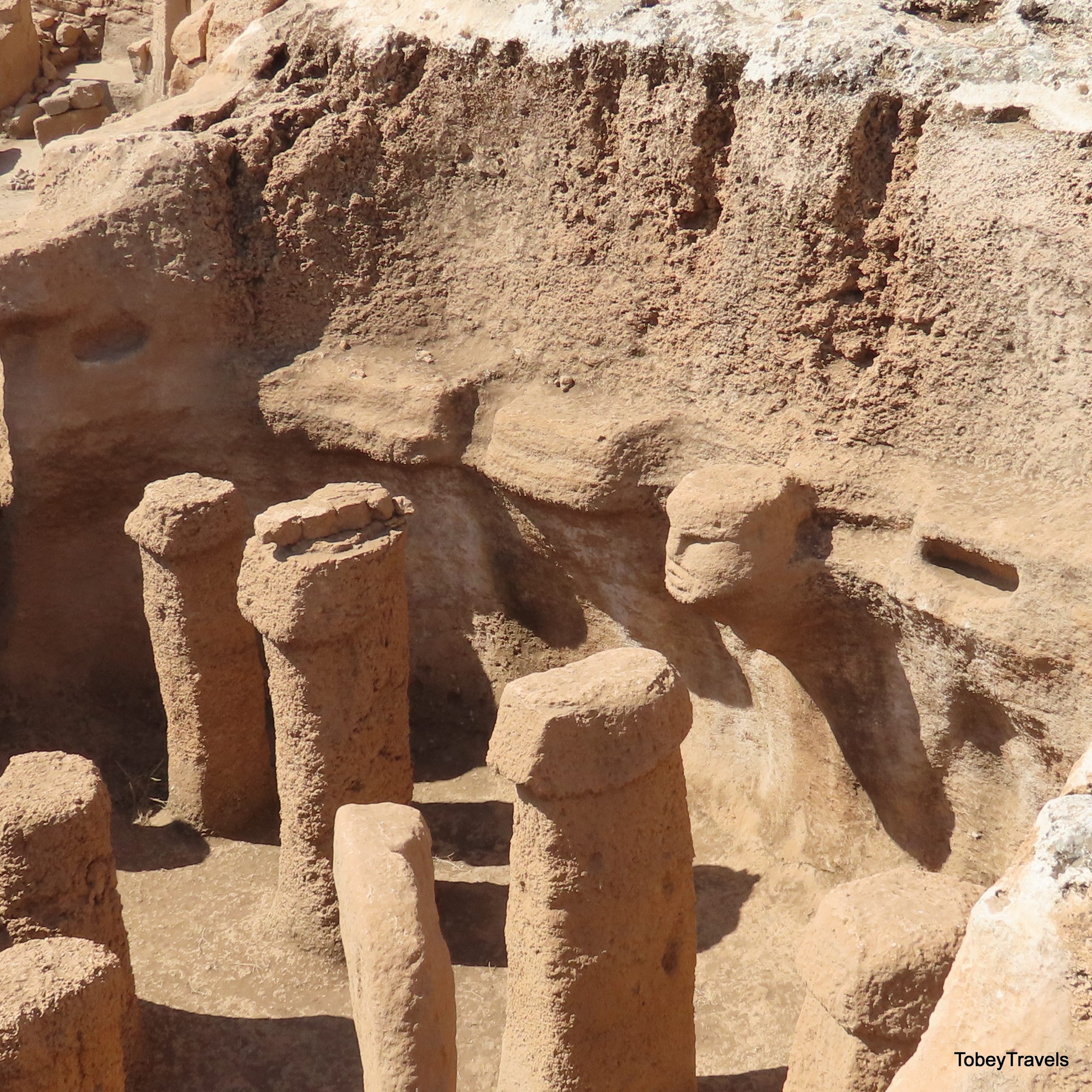 A carved human head emerging from the rock beside a porthole-like opening, part of the striking architecture at Karahan Tepe.