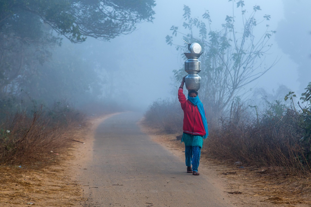 A misty country road in the hills with a villager carrying water vessels