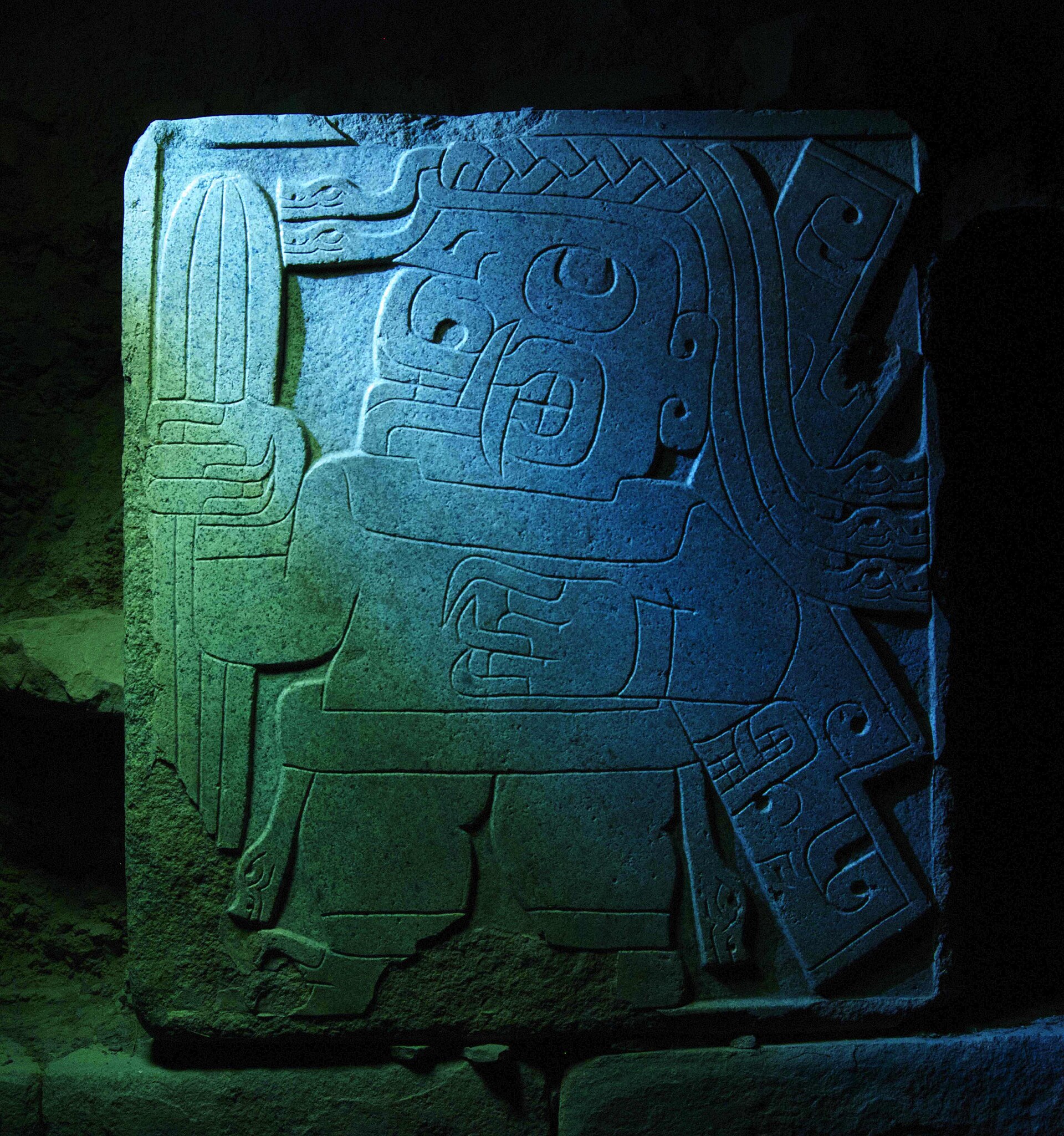 A Chavin stela carved in intricate low relief, its imagery blending human, feline, and serpent forms.