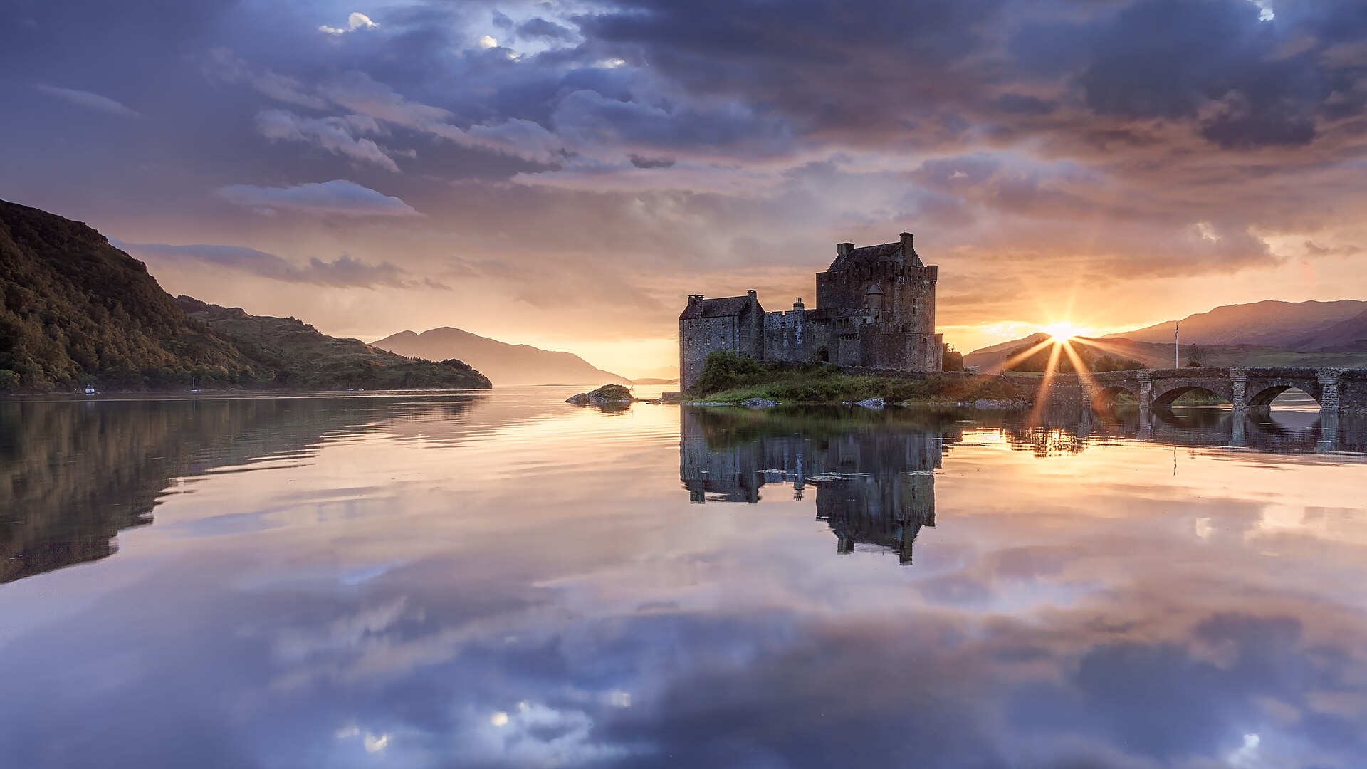Eilean Donan floodlit at dusk, its reflection shimmering across the loch