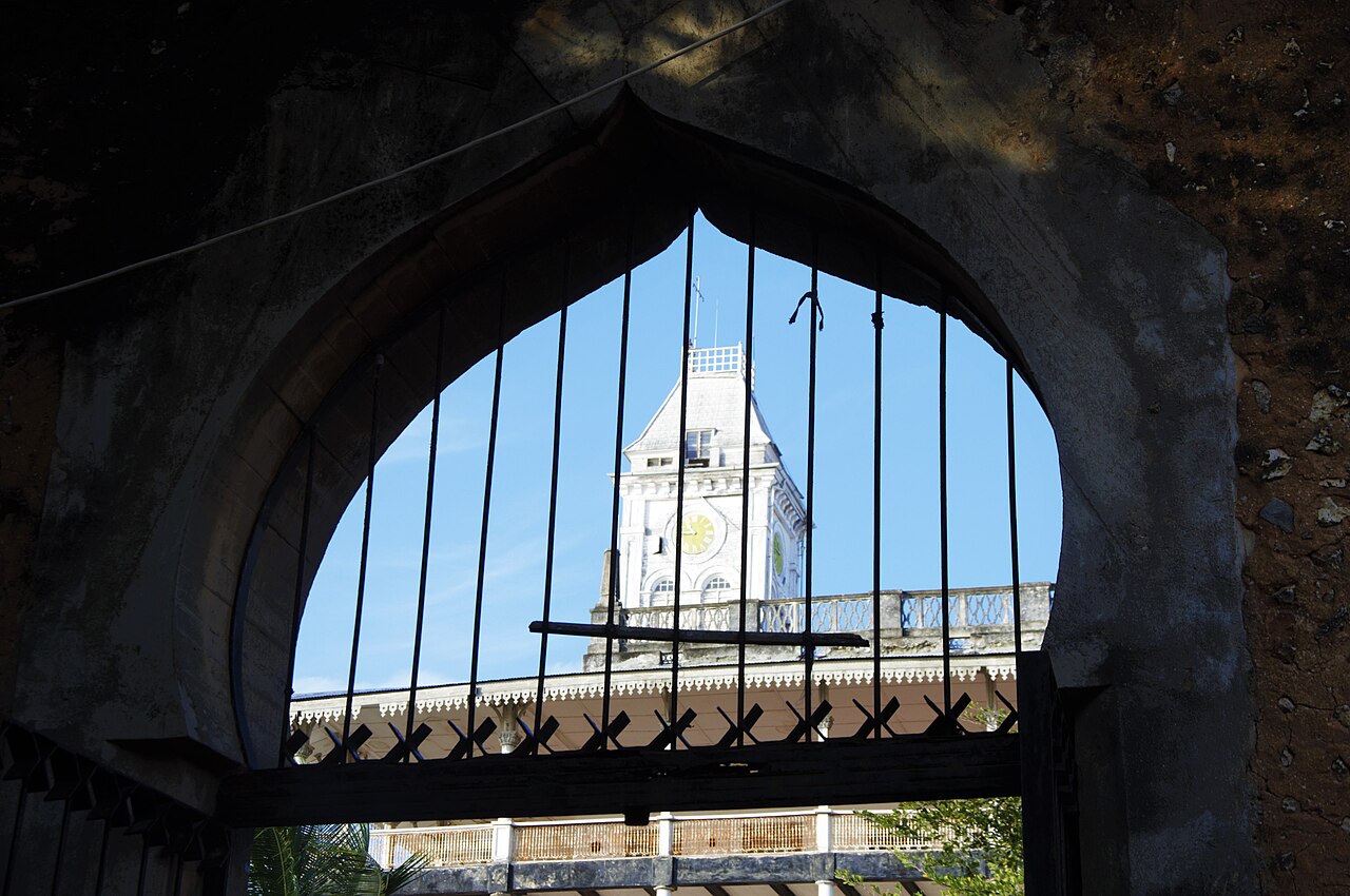 The clock tower framed through a carved Zanzibari doorway.
